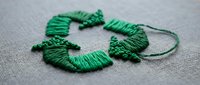 Green embroidery thread arranged in decorative loops on gray fabric background for needlework and crafting projects.