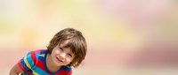 Young boy with light brown hair and fair complexion wearing colorful striped shirt, smiling at camera against soft blurred background for portrait and family use.
