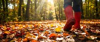 Young woman wearing red boots walking through autumn forest covered with fallen golden and orange leaves during sunny day.