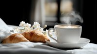 Hot cappuccino in white cup with fresh croissants and spring cherry blossoms on light textile background, morning breakfast composition with steam.