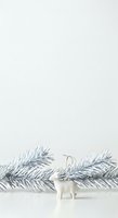 Minimalist holiday composition featuring white ceramic reindeer figurine with silver antler ornament between frosted evergreen branches on neutral background for seasonal design projects.