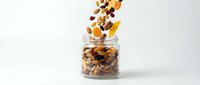 Granola and dried fruits pouring into glass jar on white background, isolated for packaging, recipe, nutrition, and healthy breakfast design use.