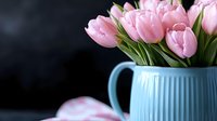 Fresh pink tulips arranged in blue ceramic pitcher against dark background for spring home decor and floral design projects.