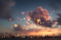 Romantic heart-shaped bokeh lights floating against dramatic sunset sky with clouds. Love concept for Valentine's Day greeting cards and wedding designs.
