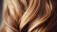 Close-up of shiny blonde and brown hair strands with highlights showing smooth texture and natural movement, suitable for hair care advertising.