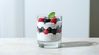 Chia seed pudding layered with fresh berries and yogurt in a glass, topped with mint leaf. Healthy dessert and breakfast option for food styling and culinary content.