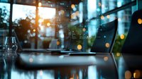 Modern office workspace with laptop and glass of water on desk, illuminated by evening sunlight creating bokeh effect through window. Atmospheric business environment.
