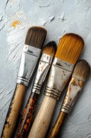 Used art brushes with paint stains and wooden handles on gray textured background, showing authentic wear and creative process in artistic workspace.