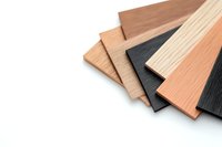 Stack of composite decking samples in various wood tones and colors including black, natural oak, and cedar shades on white background, isolated for construction projects.
