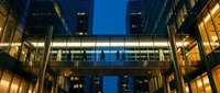 Modern office buildings with illuminated glass bridge connecting skyscrapers at twilight in urban business district creating architectural symmetry.