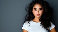 Young Asian woman with flowing dark hair and natural makeup wearing white t-shirt against dark gray background, looking confidently at camera. Professional portrait.