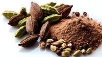 Aromatic cardamom pods and ground powder with scattered seeds on white surface, macro food photography showing texture and detail of exotic spice ingredients.
