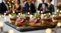 Elegant beef tenderloin crostini appetizers on slate board at upscale holiday party, garnished with herbs and cream sauce.