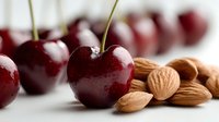 Fresh ripe cherries with stems and raw almonds on white background, healthy food combination for snacking and dessert recipes.
