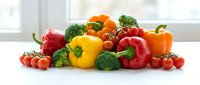Fresh colorful vegetables including bell peppers, broccoli, tomatoes and cherry tomatoes arranged on white surface for healthy cooking and nutrition.