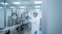 Pharmaceutical technician in sterile cleanroom operating automated production equipment for drug manufacturing and quality control processes.