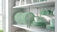 Mint green ceramic dishes neatly arranged on white kitchen shelves with chrome rack, cups hanging on hooks, bright modern home interior.