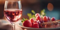 Elegant rosé wine glass with fresh strawberries and grilled meat on wooden board, perfect for romantic dinner or gourmet dining experience.