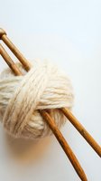 Wooden knitting needles with cream wool yarn ball on white background for crafting and handmade projects.