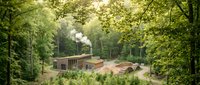 Modern industrial facility with smoking chimney nestled in lush green forest landscape for environmental impact and manufacturing concepts.