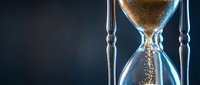 Elegant hourglass with golden sand flowing through glass bulbs on dark background symbolizing time passage, deadlines and business concepts.