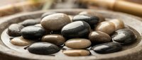 Smooth polished river stones in wooden bowl for spa relaxation massage therapy and zen meditation practices.