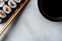 Fresh sushi rolls with rice and filling arranged on wooden plate with chopsticks and black soy sauce bowl against white background, top view with copy space.