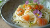Fresh salmon and capellini pasta garnished with dill and edible flowers on gray ceramic plate, elegant restaurant presentation for fine dining menus.