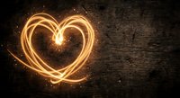 Glowing heart shape created with light trails and sparks on dark wooden background for romantic designs and Valentine's Day projects.
