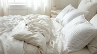 Unmade bed with white crumpled sheets and pillows in bright bedroom with natural light, suitable for home decor, lifestyle, and interior design projects.