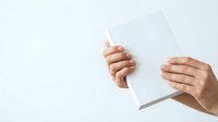 Hands holding blank white paper sheet against neutral background, suitable for mockups, presentations, advertising campaigns, and design templates.