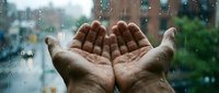 Open hands catching raindrops against wet window with urban cityscape background, symbolizing hope, renewal, gratitude and environmental awareness for seasonal or weather-related projects.