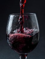 Red wine pouring into glass with dynamic splash and bubbles against dark background for beverage advertising and culinary content.