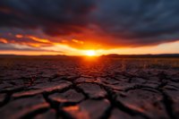 Dramatic sunset over cracked dry soil in desert, dark stormy clouds with orange sunlight breaking through, showing effects of climate change and drought.