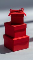 Stack of elegant red gift boxes with satin bow on top against neutral gray background, perfect for holiday, Valentine's Day or luxury retail marketing designs.