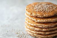Stack of homemade golden pancakes topped with sesame seeds on light background, macro food photography with selective focus and copy space.