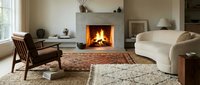 Cozy living room interior with fireplace, cream curved sofa, wooden armchair, and layered area rugs creating warm, inviting ambiance for home decor and interior design projects.