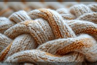 Close-up macro view of cream colored knitted wool texture with braided cable pattern showing intricate details and soft warm fabric structure.