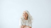 Senior woman with long white hair wearing cream sweater, smiling at camera against white background. Suitable for healthcare, wellness, lifestyle and aging gracefully concepts.