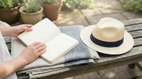 Woman hands opening blank book on wooden table with straw hat and plants in garden setting for reading relaxation and leisure outdoor lifestyle.