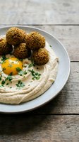 Fresh falafel balls served with creamy hummus and herbs on rustic wooden table for Mediterranean cuisine and healthy vegetarian dining concepts.