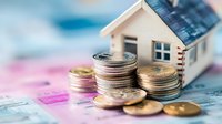 Small wooden house model with stacked coins on colorful banknotes background representing real estate investment, mortgage, property financing concept.