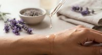 Relaxing spa treatment with lavender essential oil being applied to woman's hand in serene wellness setting with natural aromatherapy elements.