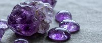 Raw amethyst crystal cluster with polished purple gemstones on linen fabric for jewelry making, healing stones, and spiritual wellness practices.