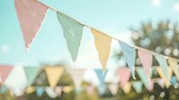 Colorful triangular bunting flags hanging outdoors against soft blue sky background for party celebration and festive decoration events.
