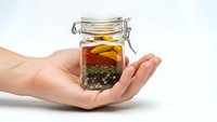 Hands holding glass jar with colorful spices including turmeric and peppercorns on white background for cooking and culinary design projects.