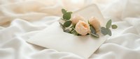 Elegant wedding invitation envelope with blush roses and eucalyptus on soft white fabric, romantic stationery for weddings and events.