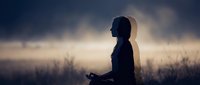 Silhouetted woman meditating in misty field at dawn, practicing mindfulness and wellness in nature for meditation, yoga, and mental health content.