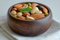 Mixed nuts and dried fruits in wooden bowl with mint leaf garnish for healthy snacking and cooking ingredients.