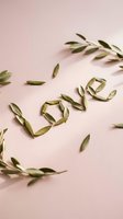 Word love spelled with green leaves on soft pink background, surrounded by scattered olive branches. Romantic nature concept for Valentine's Day.